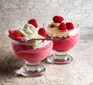 Two glasses of raspberry mousse topped with cream and raspberries