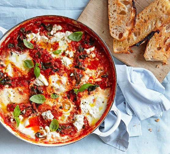 Baked eggs in a casserole dish with spinach, tomatoes, ricotta & basil