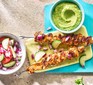 Two chicken skewers on a blue chopping board with a pot of guac and greek salad