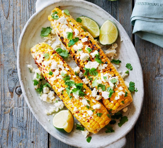 Two charred corn on the cobs topped with herbs and feta