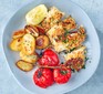 Garlic chicken on a plate with potatoes, tomatoes and a lemon wedge