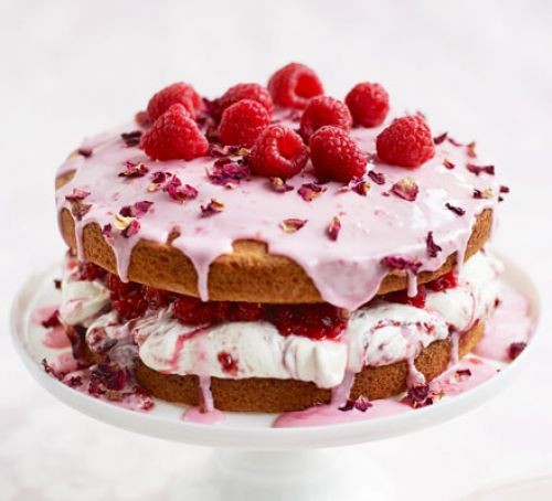 Sponge cake topped with pink icing, rose petals and raspberries