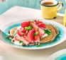 A serving of vegan strawberry pancakes on a plate with a cup of tea/coffee in the background